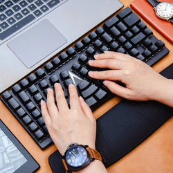 High-angle view of hands typing on a black X-Bows Nature ergonomic mechanical keyboard with wrist rest on an orange desk.